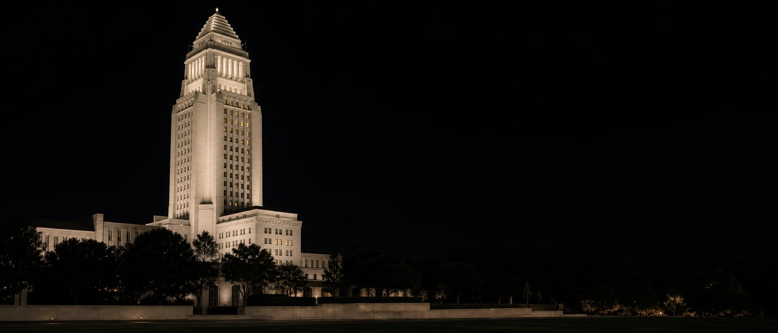 Los Angeles City Hall rises above dark civic landscaping at late dusk.