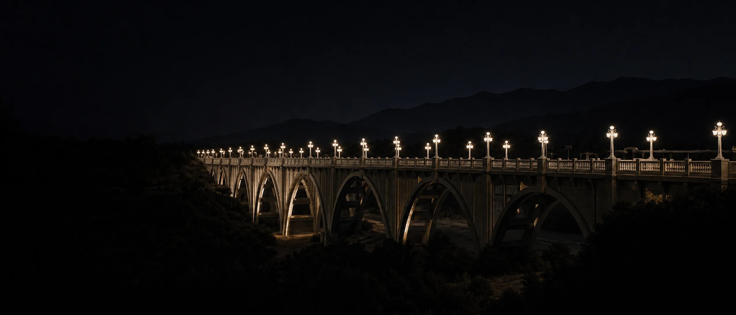 The illuminated arches of Pasadena's Colorado Street Bridge span the Arroyo Seco at blue hour.