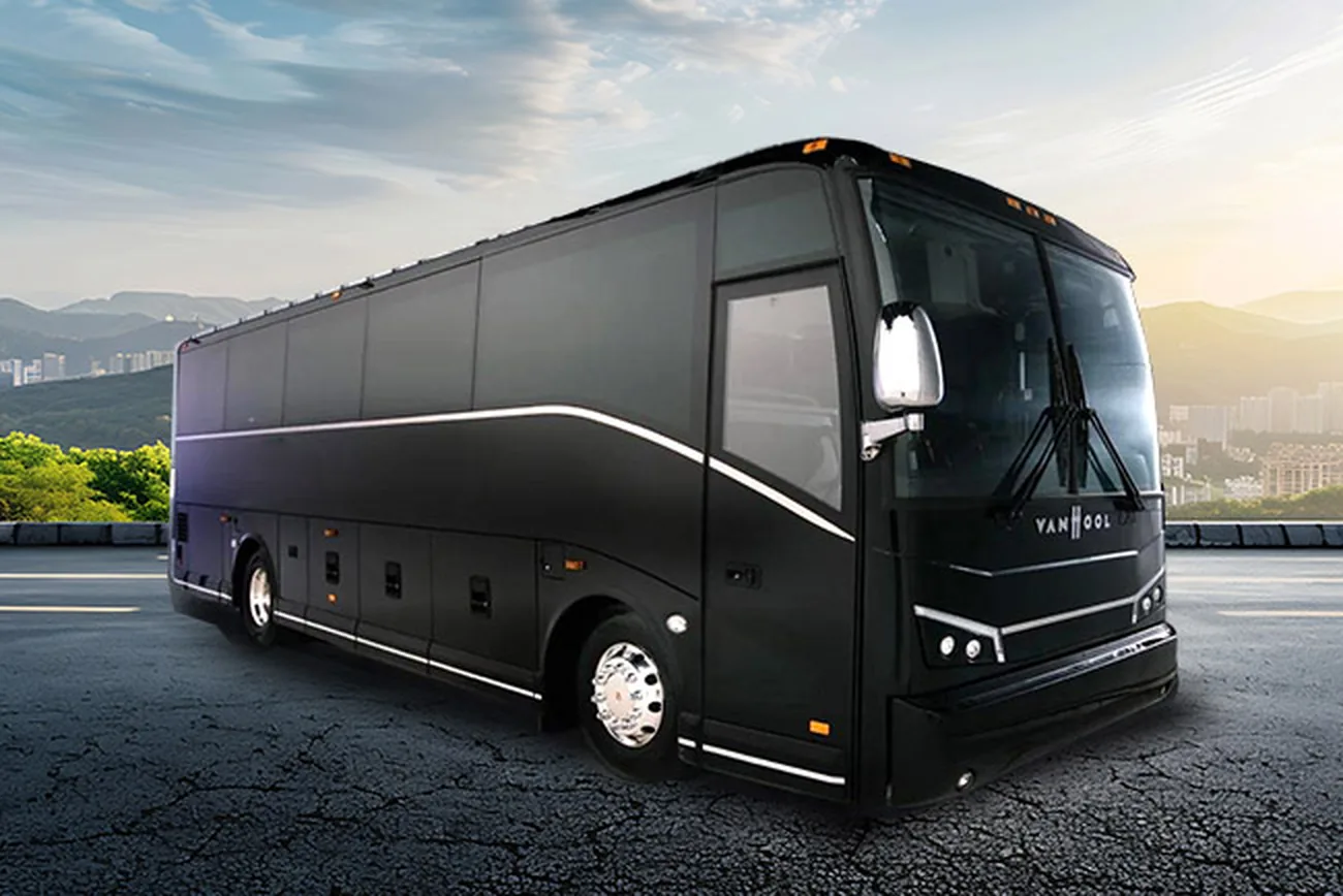 A black 40-passenger Van Hool motor coach parked on a paved mountain overlook at sunset.